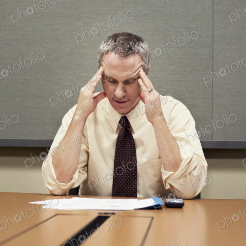 A Caucasian businessman sitting at a desk showing the stress of work.