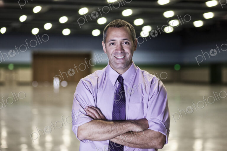 A Caucasian businessman standing in a dimly lit and dark exhibition area in a…
