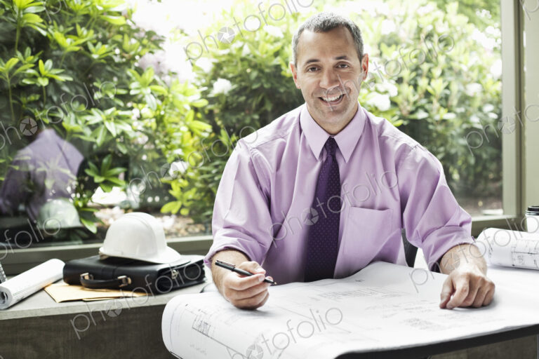 A Caucasian businessman working on architectural plans in his office.