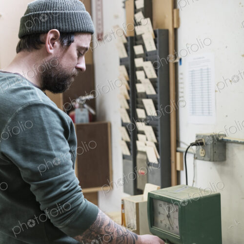 A Caucasian carpenter checking in with a time clock in a woodworking factory. A Caucasian carpenter checking in with a time clock in a woodworking factory.