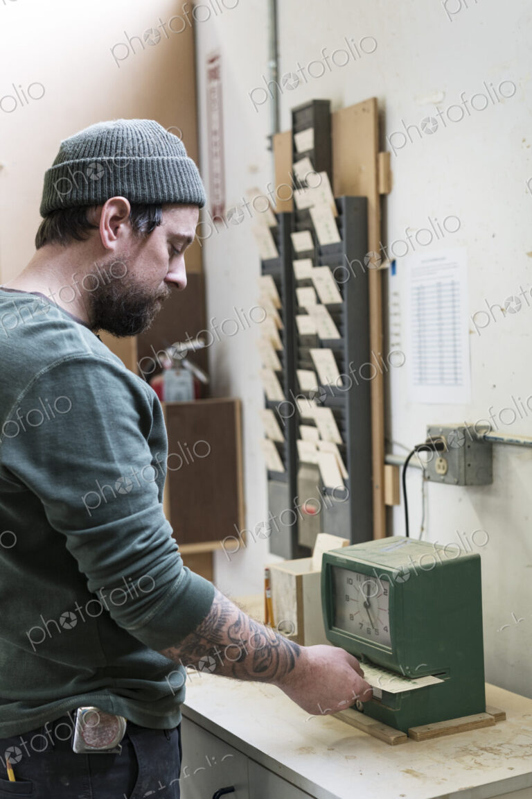 A Caucasian carpenter checking in with a time clock in a woodworking factory.