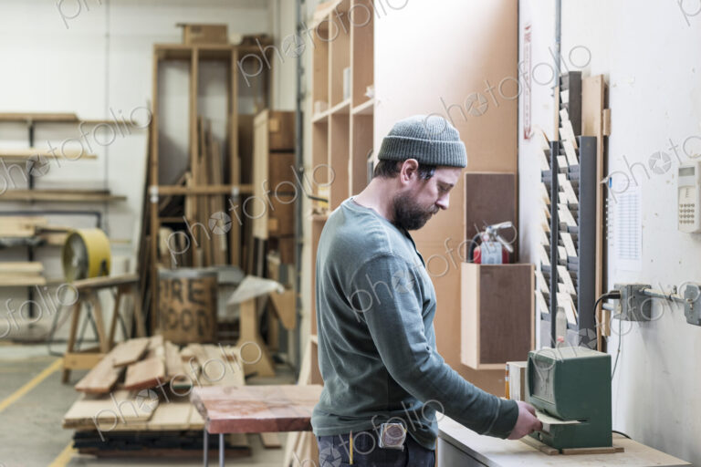 A Caucasian carpenter checking in with a time clock in a woodworking factory.