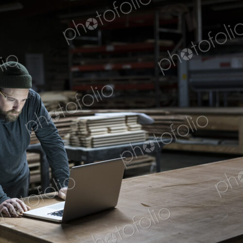 A Caucasian carpenter working on his lap top after hours in a large woodworking factory. A Caucasian carpenter working on his lap top after hours in a large woodworking factory.
