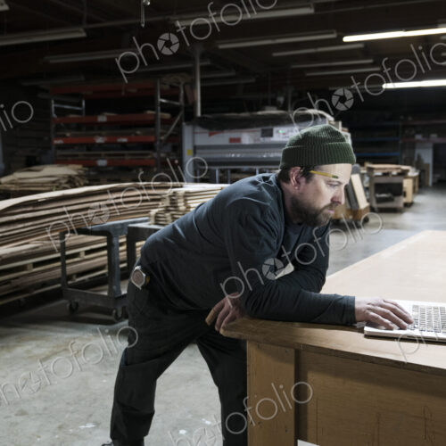 A Caucasian carpenter working on his lap top after hours in a large woodworking factory. A Caucasian carpenter working on his lap top after hours in a large woodworking factory.