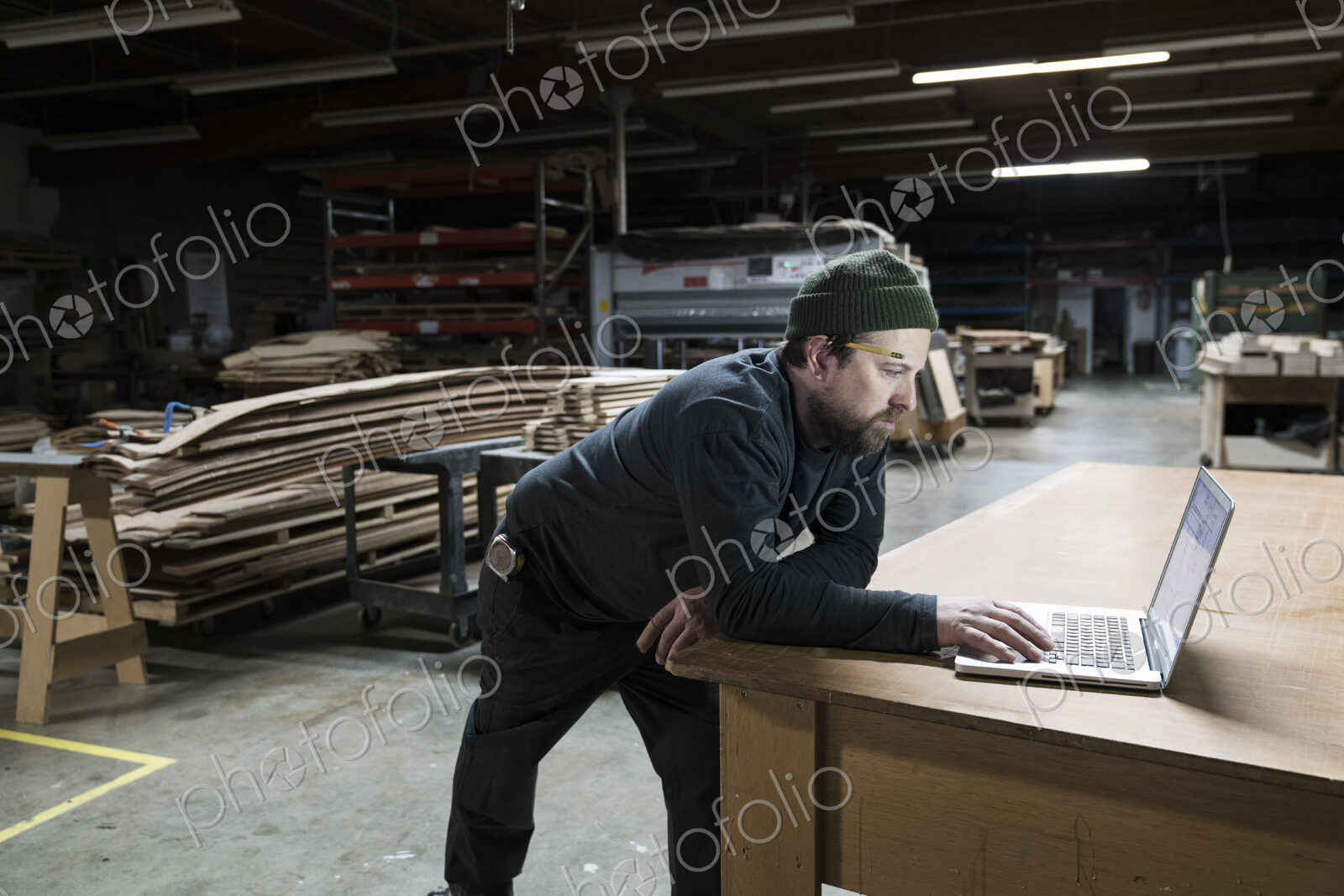 A Caucasian carpenter working on his lap top after hours in a large woodworking factory.