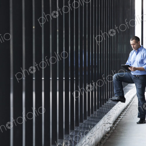 A Caucasian male architect standing by a wall of windows, using a digital tablet. A Caucasian male architect standing by a wall of windows, using a digital tablet.