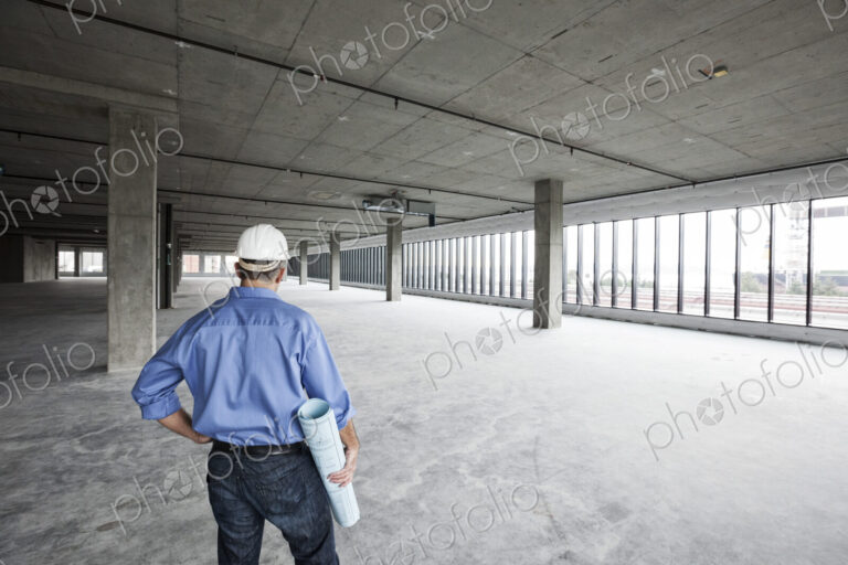 A Caucasian male architect standing looking out over a new raw business space.
