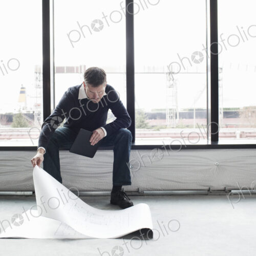 A Caucasian male architect working on building plans in a new raw business space. A Caucasian male architect working on building plans in a new raw business space.