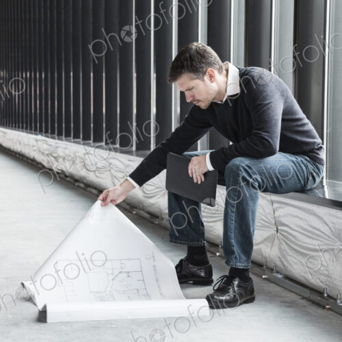 A Caucasian male architect working on building plans in a new raw business space. A Caucasian male architect working on building plans in a new raw business space.