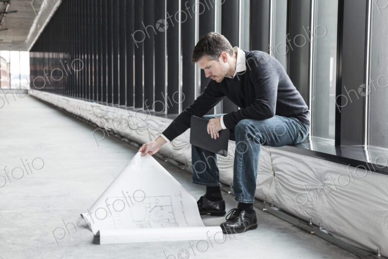 A Caucasian male architect working on building plans in a new raw business space.