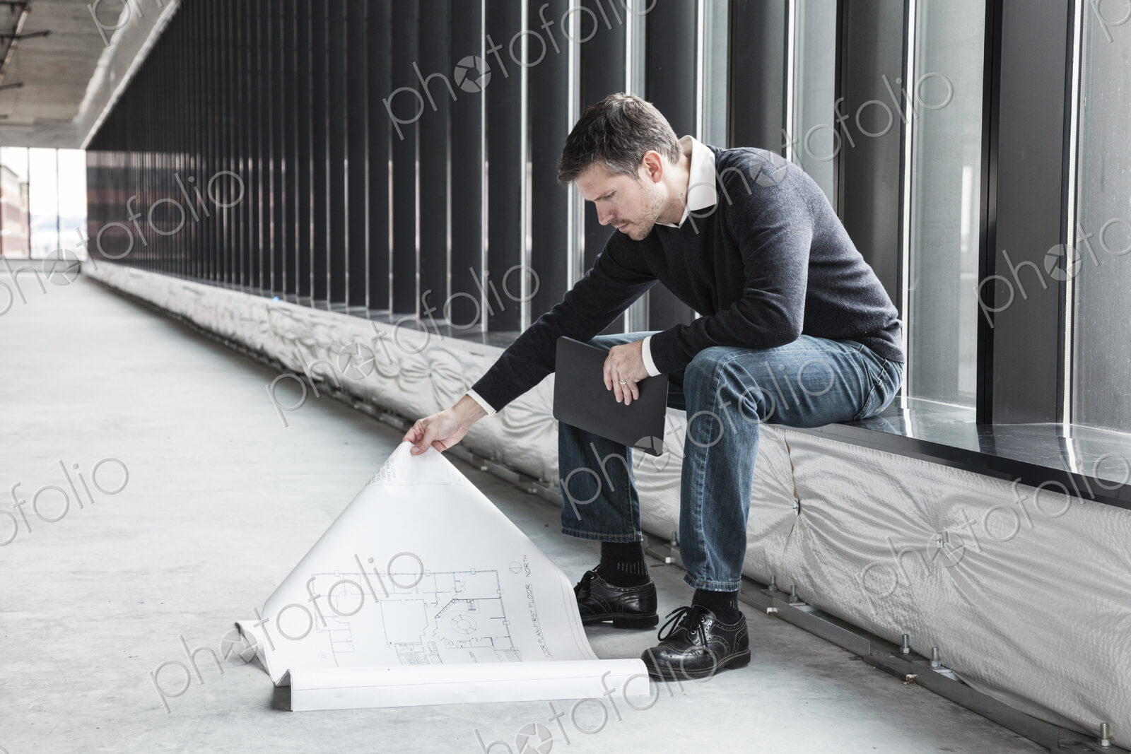 A Caucasian male architect working on building plans in a new raw business space.