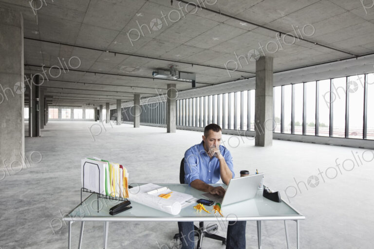 A Caucasian male business owner at his temporary desk in a new raw business space.