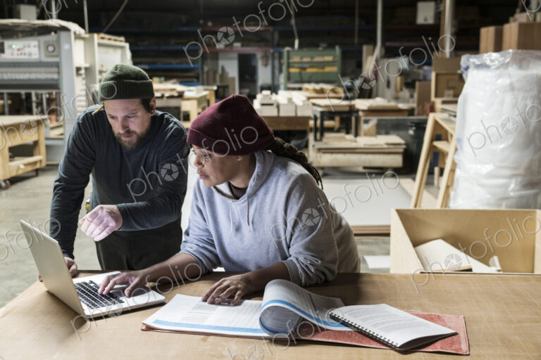 A Caucasian male carpenter and a Black female carpenter working on a laptop computer…