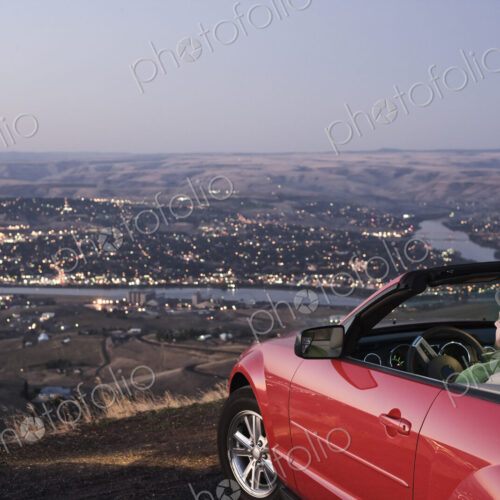 A Caucasian male parked in his convertible sports car watching the sunset over the…