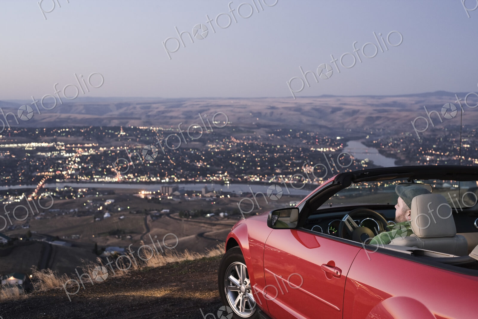 A Caucasian male parked in his convertible sports car watching the sunset over the…