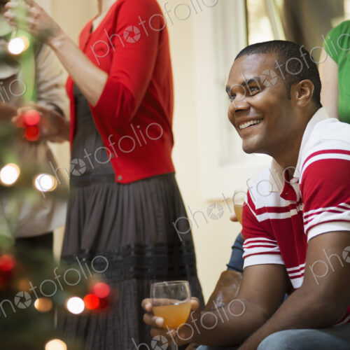A Christmas gathering, adults and children in a room around a Christmas tree,… A Christmas gathering, adults and children in a room around a Christmas tree,…
