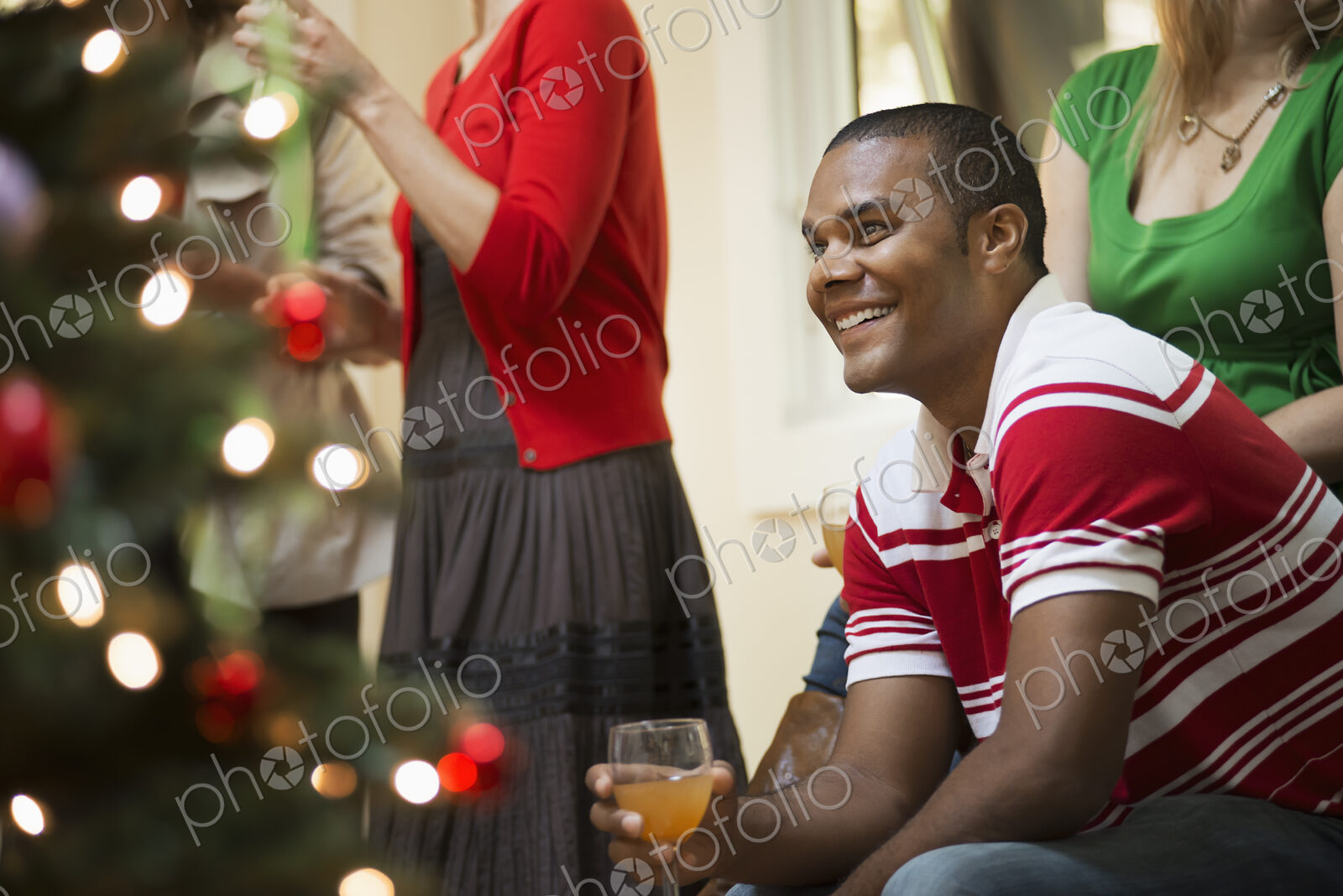 A Christmas gathering, adults and children in a room around a Christmas tree,…