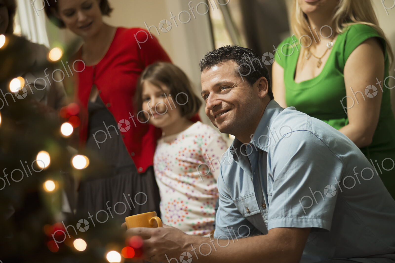 A Christmas gathering, adults and children in a room around a Christmas tree,…