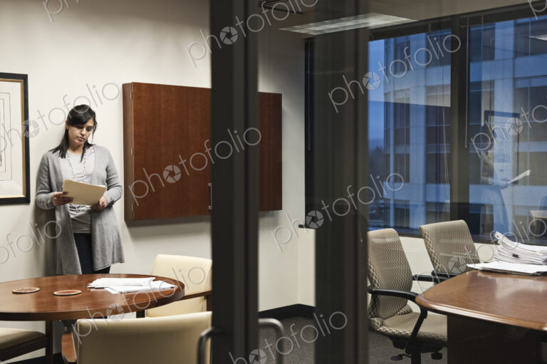 A Mixed Race woman working in an office, viewed through a glass doorway.