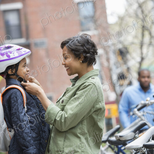 A New York city park in the spring. A boy in a cycle helmet, being fastened by his…