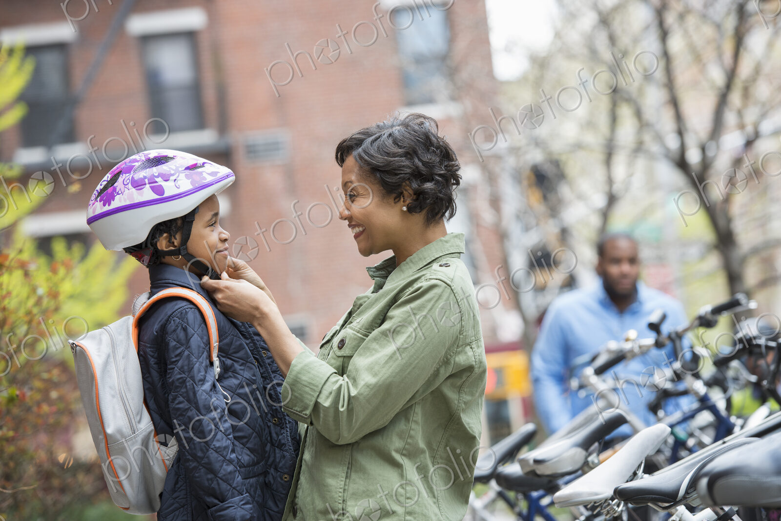A New York city park in the spring. A boy in a cycle helmet, being fastened by his…