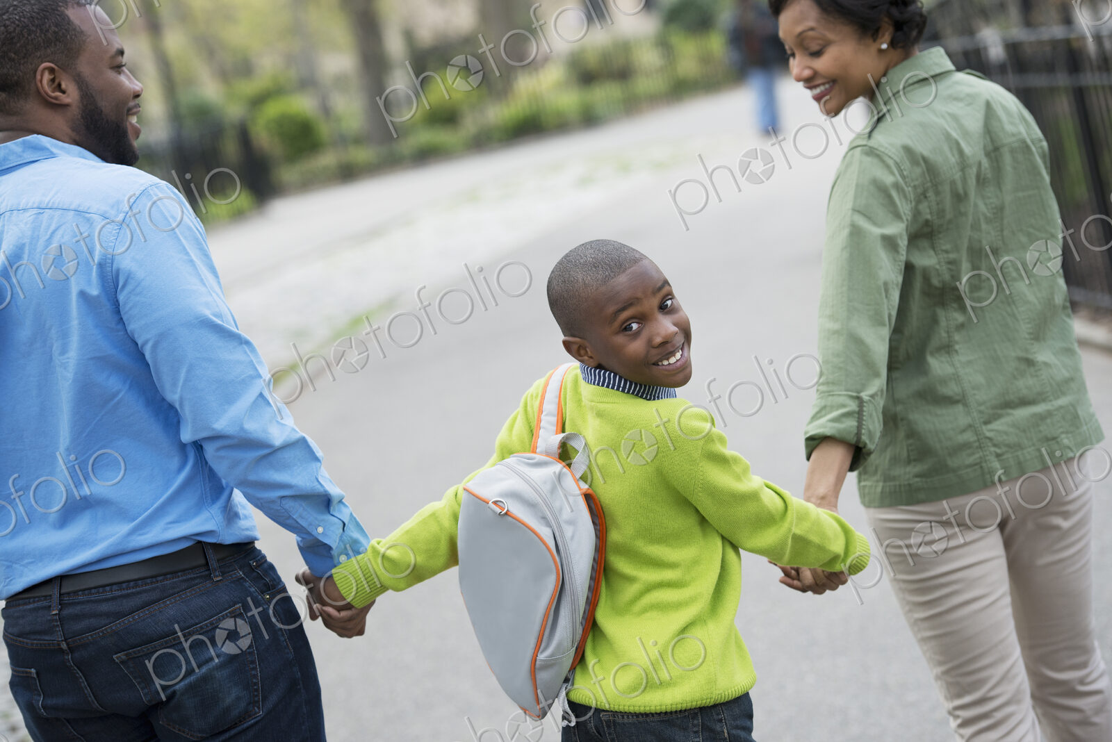 A New York city park in the spring. A boy with a bookbag, holding hands with his…