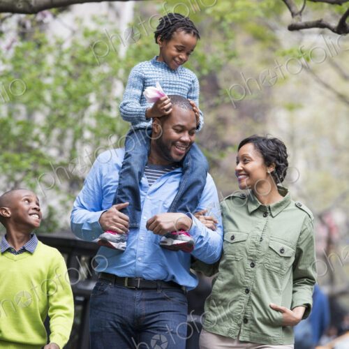 A New York city park in the spring. A family, parents and two boys. A child riding on… A New York city park in the spring. A family, parents and two boys. A child riding on…