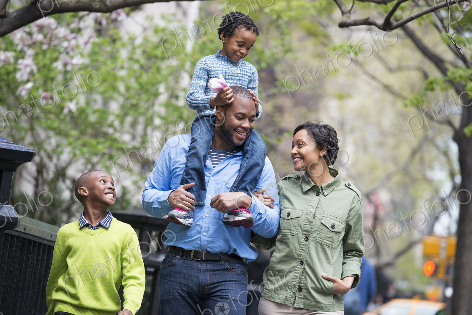 A New York city park in the spring. A family, parents and two boys. A child riding on…