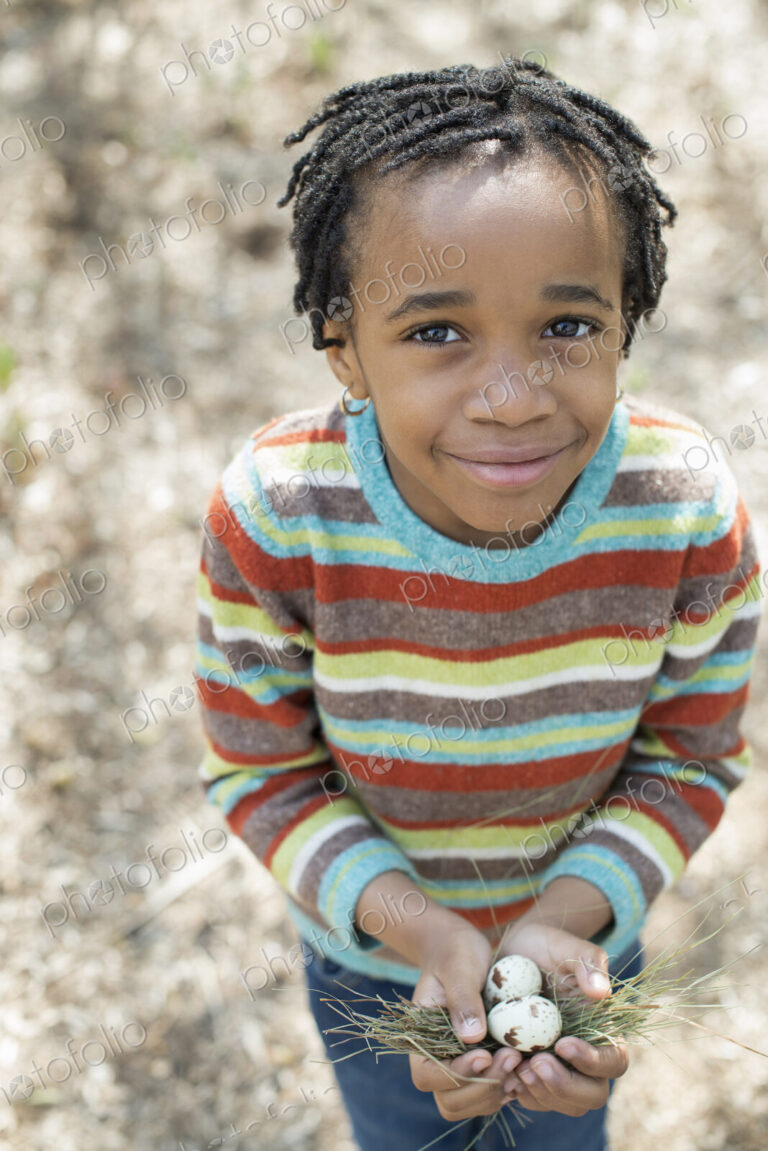 A New York city park in the spring. A small boy in a striped shirt, holding a nest…
