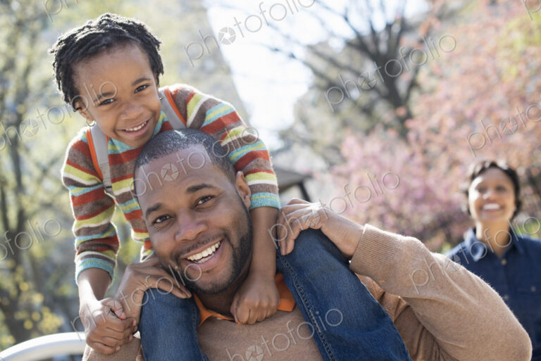 A New York city park in the spring. Sunshine and cherry blossom. A father carrying his…