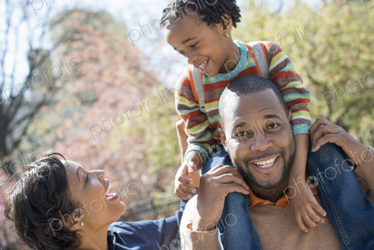 A New York city park in the spring. Sunshine and cherry blossom. A father carrying his…