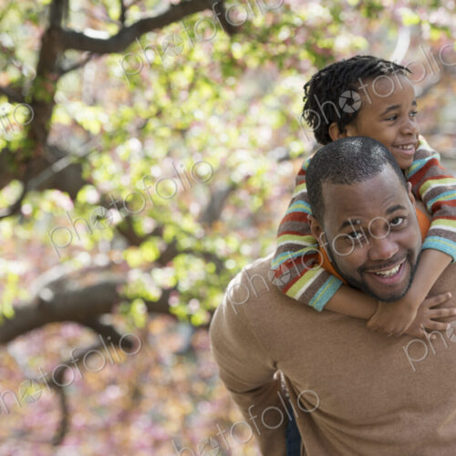 A New York city park in the spring. Sunshine and cherry blossom. A father carrying his…