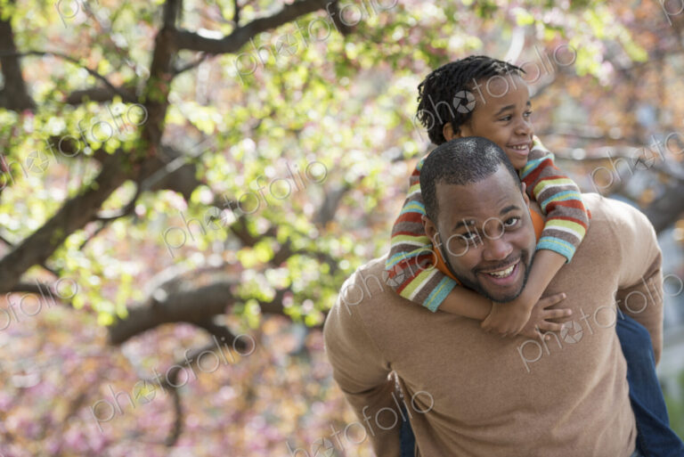 A New York city park in the spring. Sunshine and cherry blossom. A father carrying his…