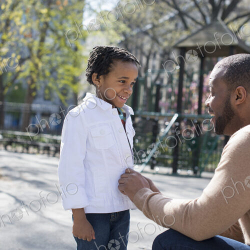 A New York city park in the spring. Sunshine and cherry blossom. A father kneeling and…