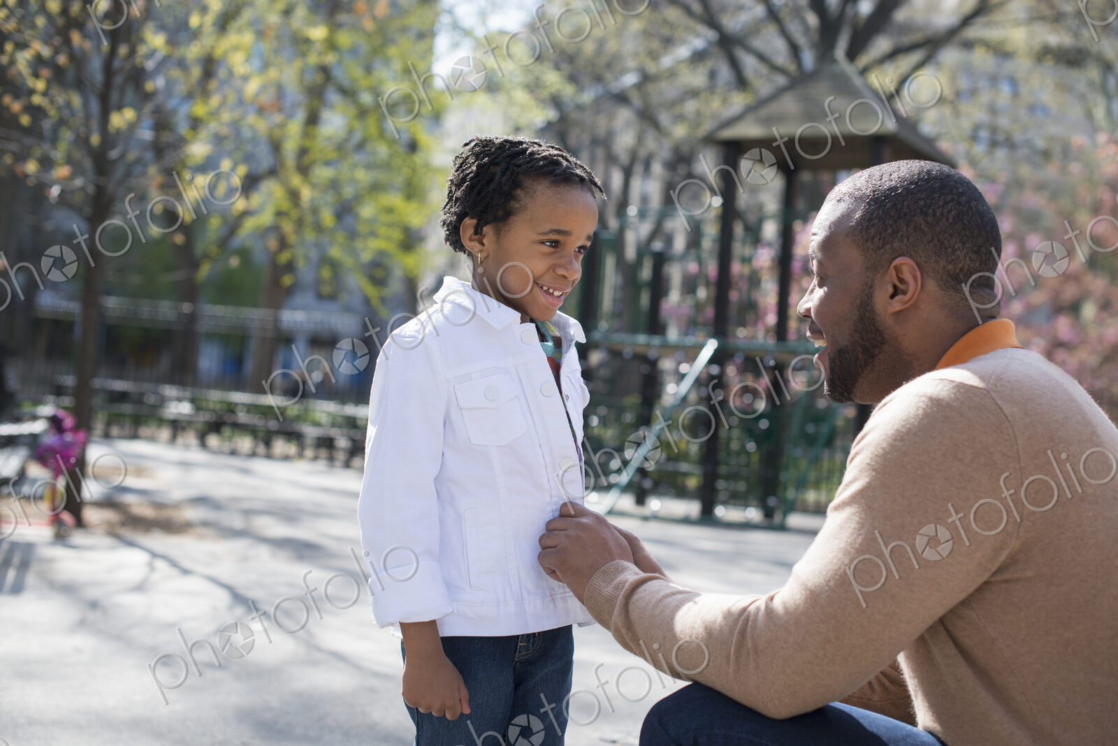 A New York city park in the spring. Sunshine and cherry blossom. A father kneeling and…