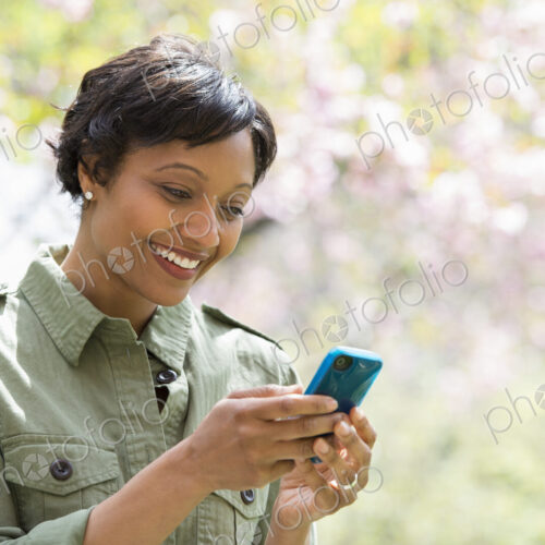 A New York city park in the spring. Sunshine and cherry blossom. A woman checking her… A New York city park in the spring. Sunshine and cherry blossom. A woman checking her…