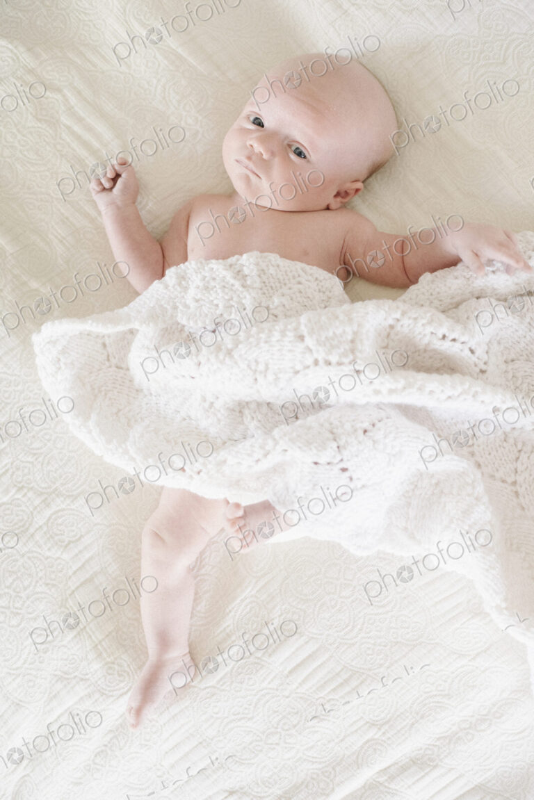 A baby boy lying on his back on a bed.