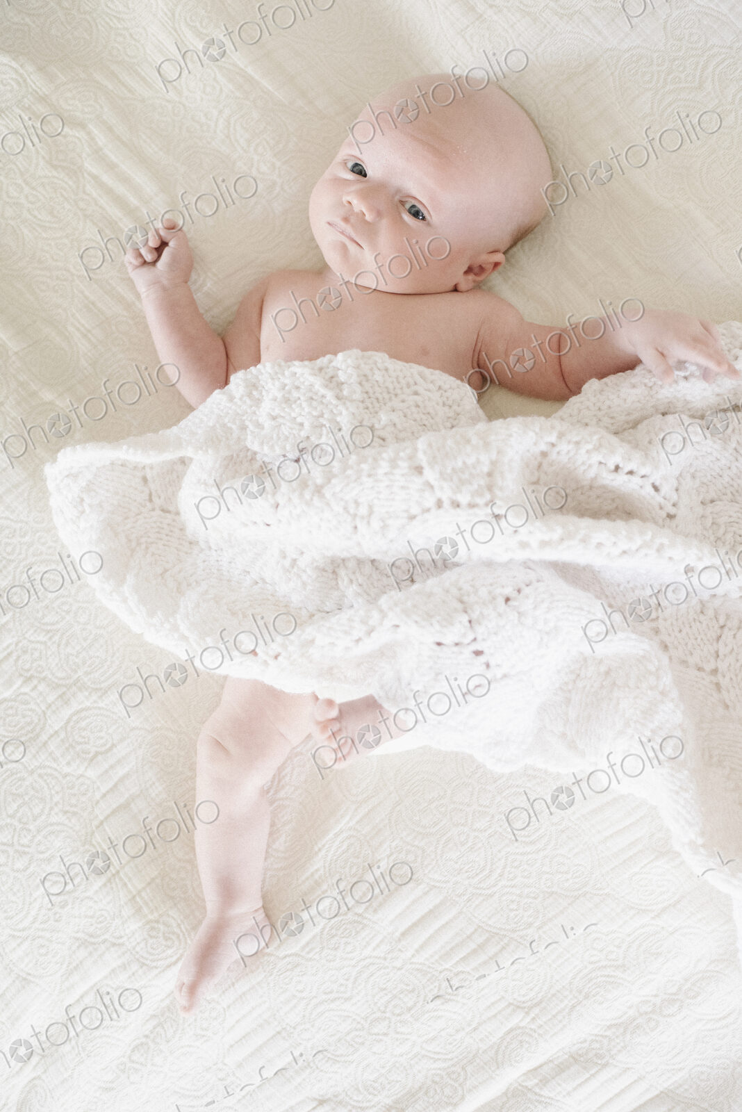 A baby boy lying on his back on a bed.