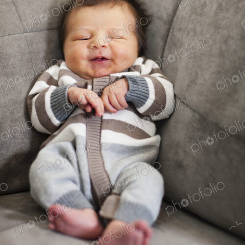 A baby propped up in the corner of a sofa.