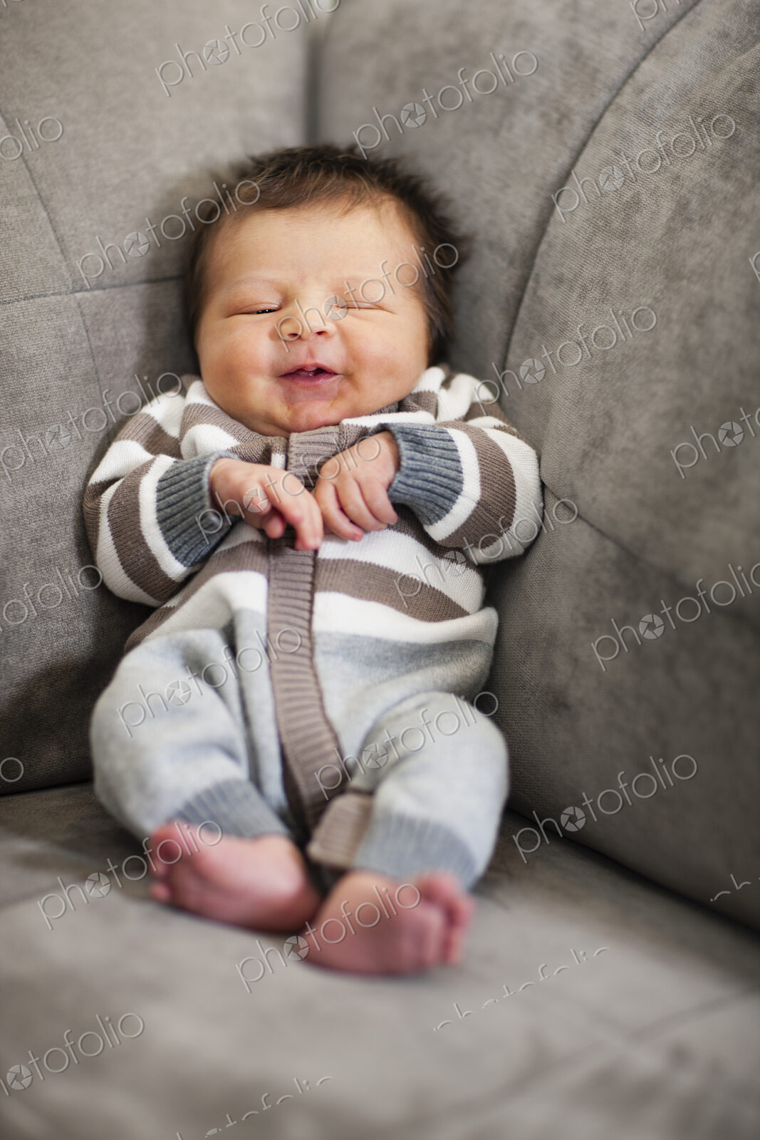 A baby propped up in the corner of a sofa.