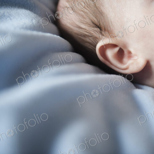 A baby's head and ear, against a blue bedsheet. A baby's head and ear, against a blue bedsheet.