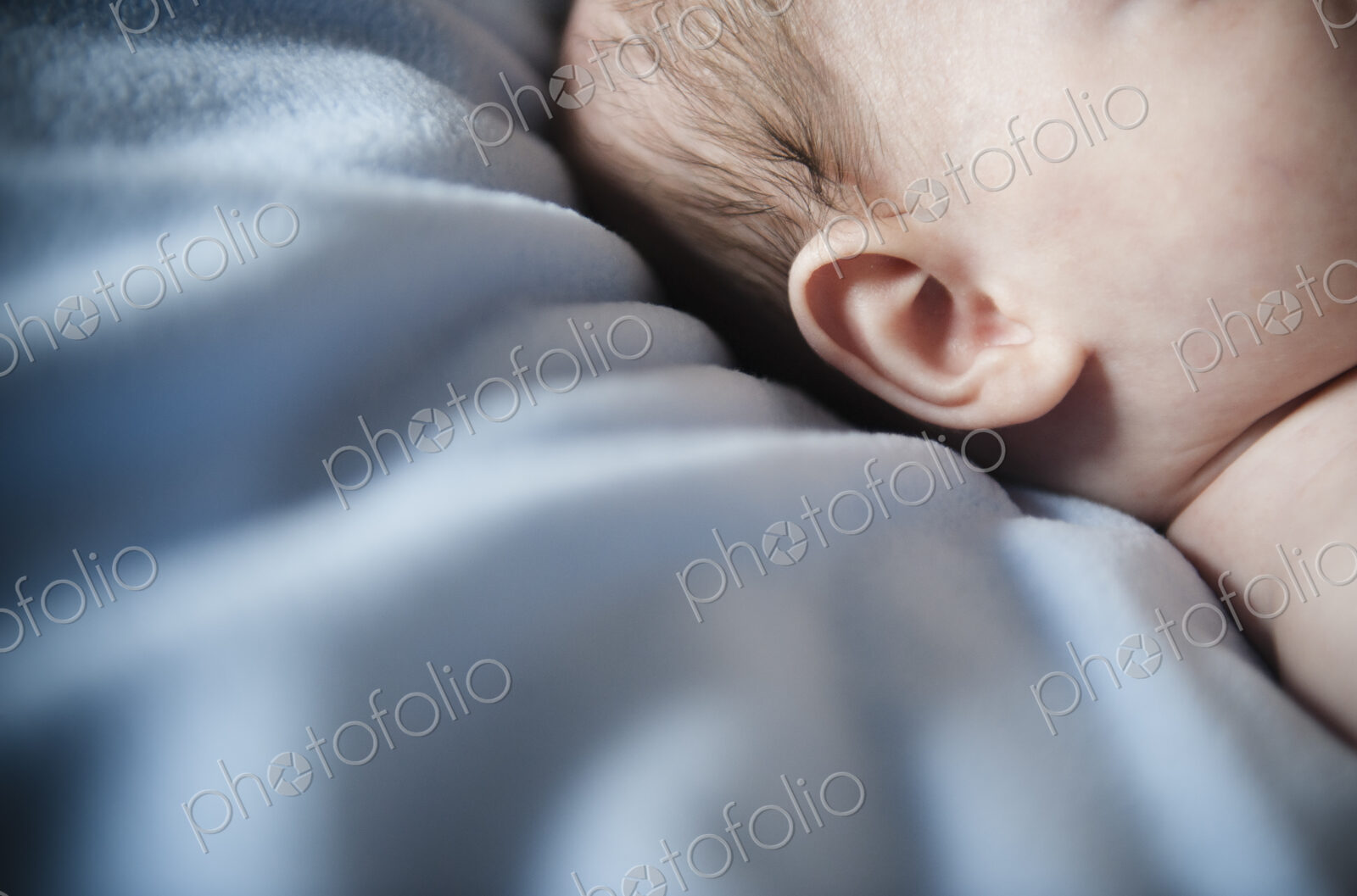 A baby’s head and ear, against a blue bedsheet.