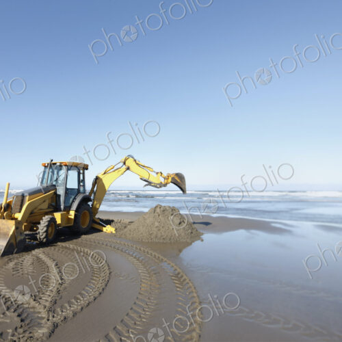 A backhoe, digger with large scoop working on the soft sand at the water's edge. A backhoe, digger with large scoop working on the soft sand at the water's edge.