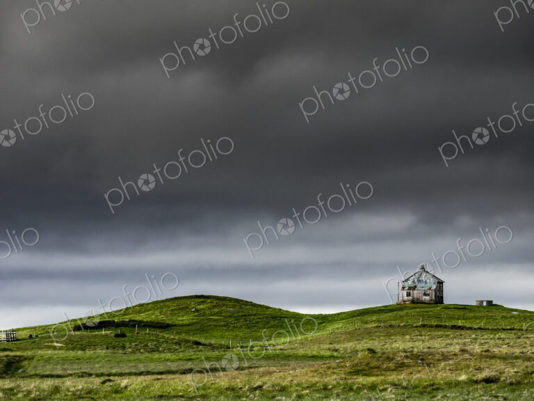 A barn on the crest of a hill, and dark storm clouds glowering over the land.