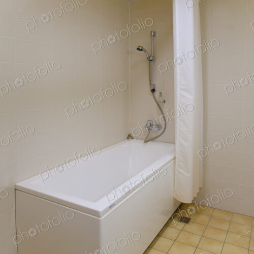 A bathroom, bathtub and wall mounted shower and shower curtain, tiled floor and yellow…