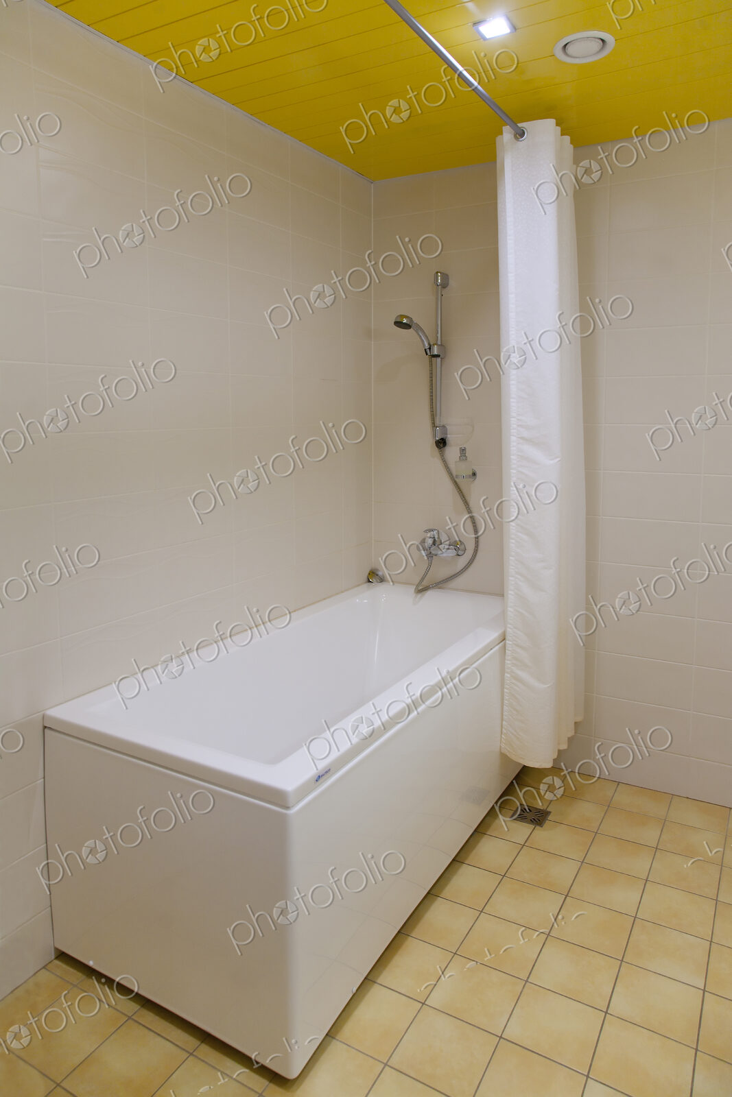 A bathroom, bathtub and wall mounted shower and shower curtain, tiled floor and yellow…