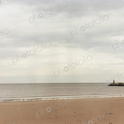 A beach and view to the end of a pier jutting out into the sea.