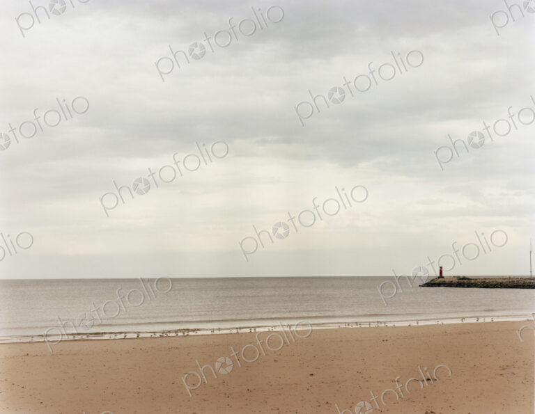 A beach and view to the end of a pier jutting out into the sea.