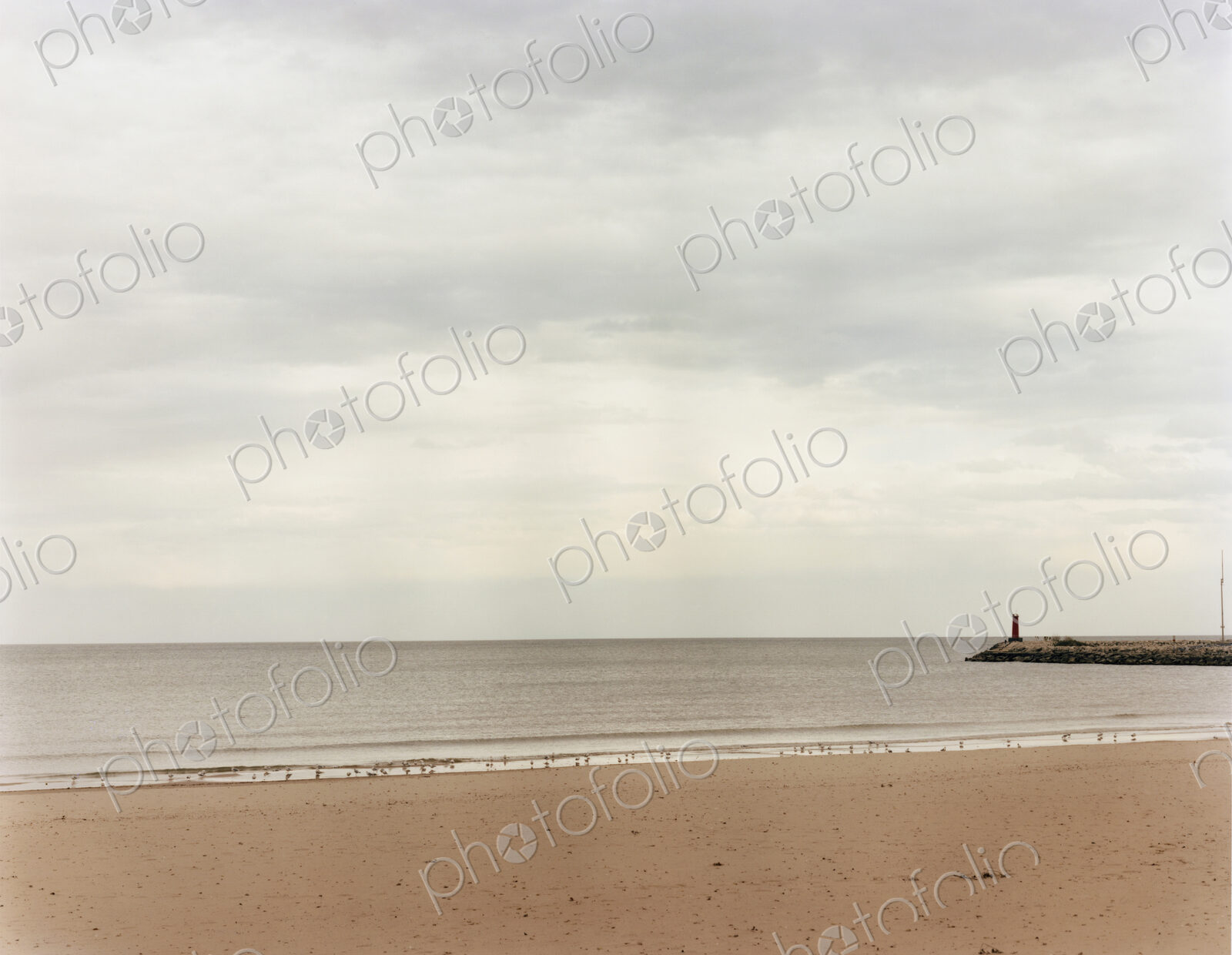 A beach and view to the end of a pier jutting out into the sea.