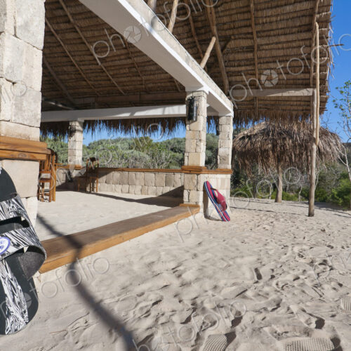 A beach resort building on a white sand beach, a pair of flipflops on the steps of a…